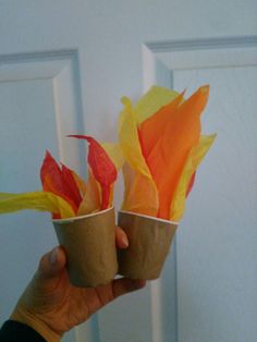 someone holding two paper cups with orange and yellow flowers in them