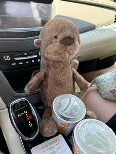 a teddy bear sitting in the center console of a car next to cans of soda