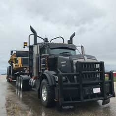 a large black truck parked on top of a wet parking lot next to a yellow dump truck