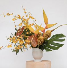 a white vase filled with yellow flowers and pineconi on top of a wooden stand