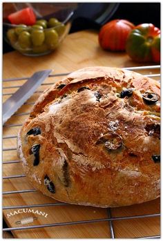 a loaf of bread sitting on top of a cooling rack next to a knife and bowl of fruit