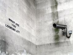 a security camera on the side of a building with graffiti written on it that says, what are you looking at?