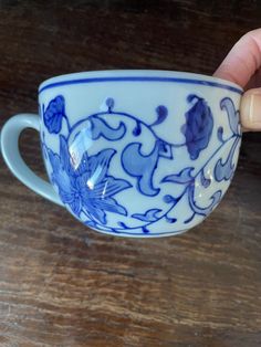 a hand holding a blue and white cup on top of a wooden table