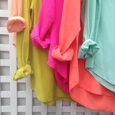 there are many different colored shirts hanging on the clothes rack in front of a white fence