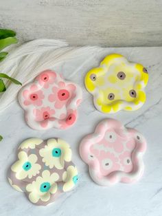 four flower shaped buttons sitting on top of a white table next to green leaves and a potted plant