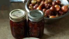 two jars filled with jam sitting on top of a table next to a bowl of fruit