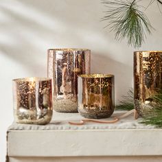 three gold colored candles sitting on top of a white mantle next to a pine tree