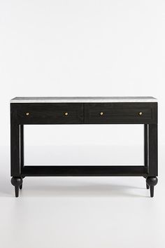 a black console table with two drawers and gold knobs on the bottom, against a white background