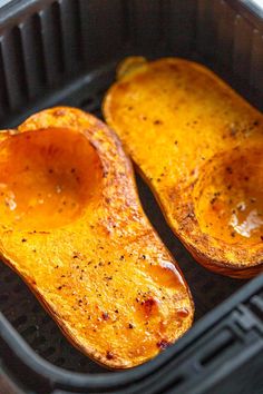 two squash halves in a black plastic container with some seasoning on the top and bottom