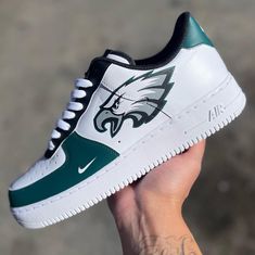 a hand holding a white and green nike air force shoe with the philadelphia eagles logo on it