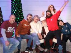 a group of people sitting next to each other in front of a christmas tree with lights