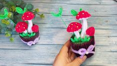 someone is holding two small knitted mushrooms in front of a potted plant on a wooden table