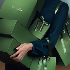 a woman is holding several green boxes with the word la mer written on them in cursive writing