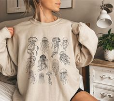 This jellyfish sweater with a jellyfish print is perfect for an ocean inspired style and summer sweatshirt for animal, marine life, sea and nature lovers. It's a great gift for marine biologists. Also available as T-Shirt: https://wandercraftsdesign.etsy.com/listing/1728681053/save-the-ocean-inspired-style-jellyfish ♥PRODUCTION TIME: 1-5 days (usually 2-3 days) ♥SHIPPING TIME: 2-5 days in USA (Usually 2-3 days). International shipping takes longer. ♥PRODUCT DESCRIPTION: Gildan 18000 Unisex Sweat Jellyfish Sweater, Work Appropriate Costumes, Jellyfish Shirt, Sweater Print, Save The Ocean, Jellyfish Print, Summer Sweatshirt, Animal Nature, Ocean Inspired