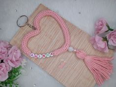 a pink heart shaped keychain sitting on top of a wooden board next to flowers