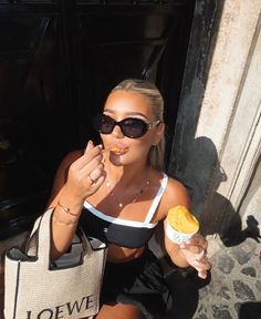 a woman sitting on the ground eating an ice cream cone and holding a tote bag