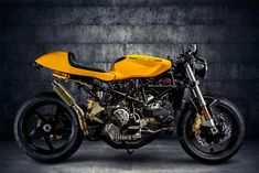 a yellow and black motorcycle is parked in a dark room with concrete walls behind it