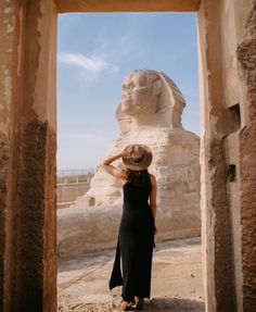 a woman wearing a hat standing in front of an ancient sphinx statue at the giza museum