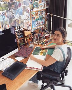 a woman sitting at a desk in front of a computer monitor with pictures on the wall behind her