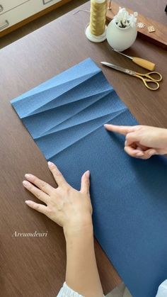 two hands pointing at blue paper on a table with scissors and other crafting supplies