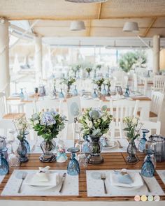 the table is set with blue and white flowers in vases, plates and napkins