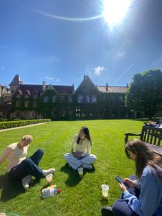 four people sitting on the grass in front of a building with a sun shining over them