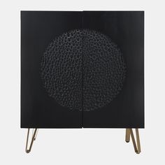 a black cabinet with gold legs and a circular design on the front, against a white background