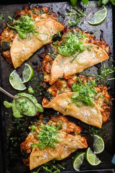 some tacos are sitting on a tray with limes and cilantro sauce