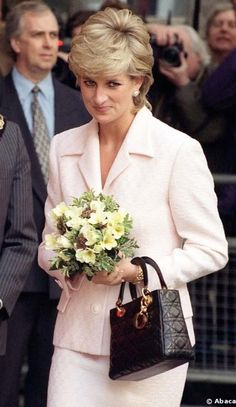 the woman is holding a bouquet of flowers in her hand while walking down the street