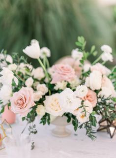 an arrangement of white and pink flowers in a vase on a table with greenery