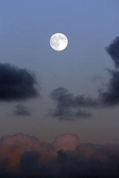 the moon is shining brightly in the sky above some dark clouds and blue sky with white fluffy clouds