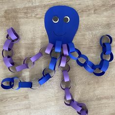 an octopus made out of purple paper on top of a wooden floor with chains attached to it