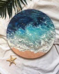 an ocean scene painted on top of a white sheet next to a starfish and palm leaf