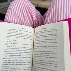 an open book sitting on top of a bed next to a pink and white pillow