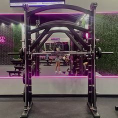 a gym with purple lighting and people doing squats in the background is a mirror