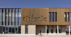 a person walking in front of a building with wooden slats on the facade and windows