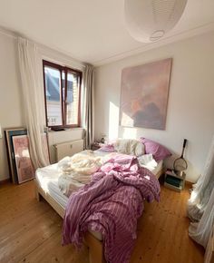 an unmade bed with pink sheets and blankets on it in front of a window