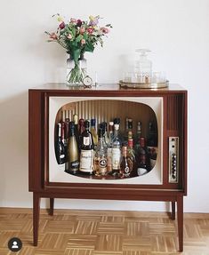 an entertainment center with liquor bottles and flowers on the top shelf, in front of a white wall