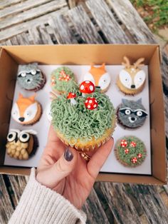 a person is holding up a cupcake with green frosting and red mushrooms on it