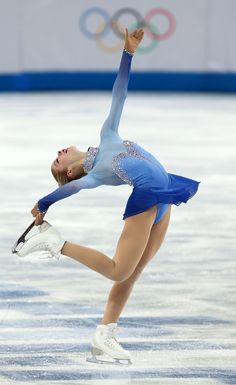 a female figure skating on the ice in a blue dress and white shoes with her arms outstretched