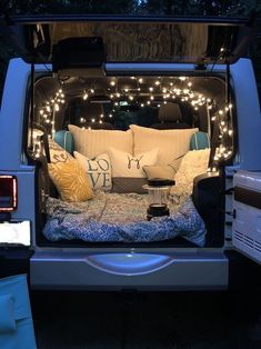 the back end of a van with pillows and lights in the bed area, parked at night