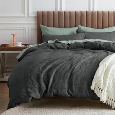 a bed with grey and green comforters in a white room next to a brown headboard