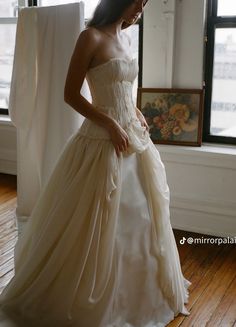 a woman in a wedding dress standing by a window with her hands on her hips