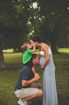 a man kneeling down next to a woman holding a child on his shoulders and kissing her cheek