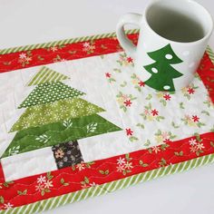 a coffee cup on top of a place mat with a christmas tree design in the center