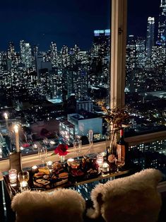 a dining table with candles on it in front of a window overlooking the city at night