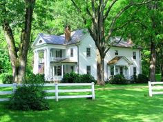 a large white house sitting in the middle of a lush green field next to trees