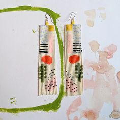 two pairs of beaded earrings on top of a piece of paper with green paint