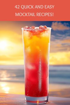 a tall glass filled with liquid and ice on top of a table next to the ocean