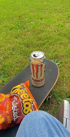 a person sitting on top of a skateboard next to a bag of chips and drink